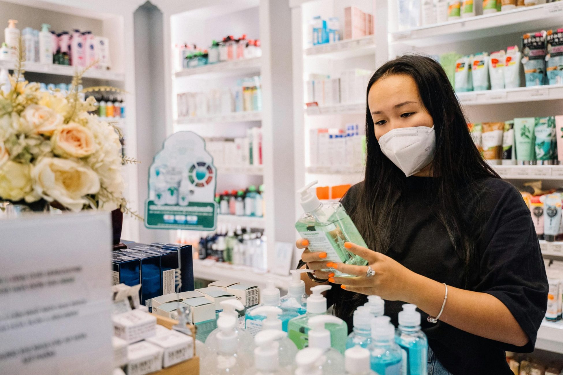 Frau mit FFP2 Maske steht in Apotheke und begutachtet Kosmetikprodukte